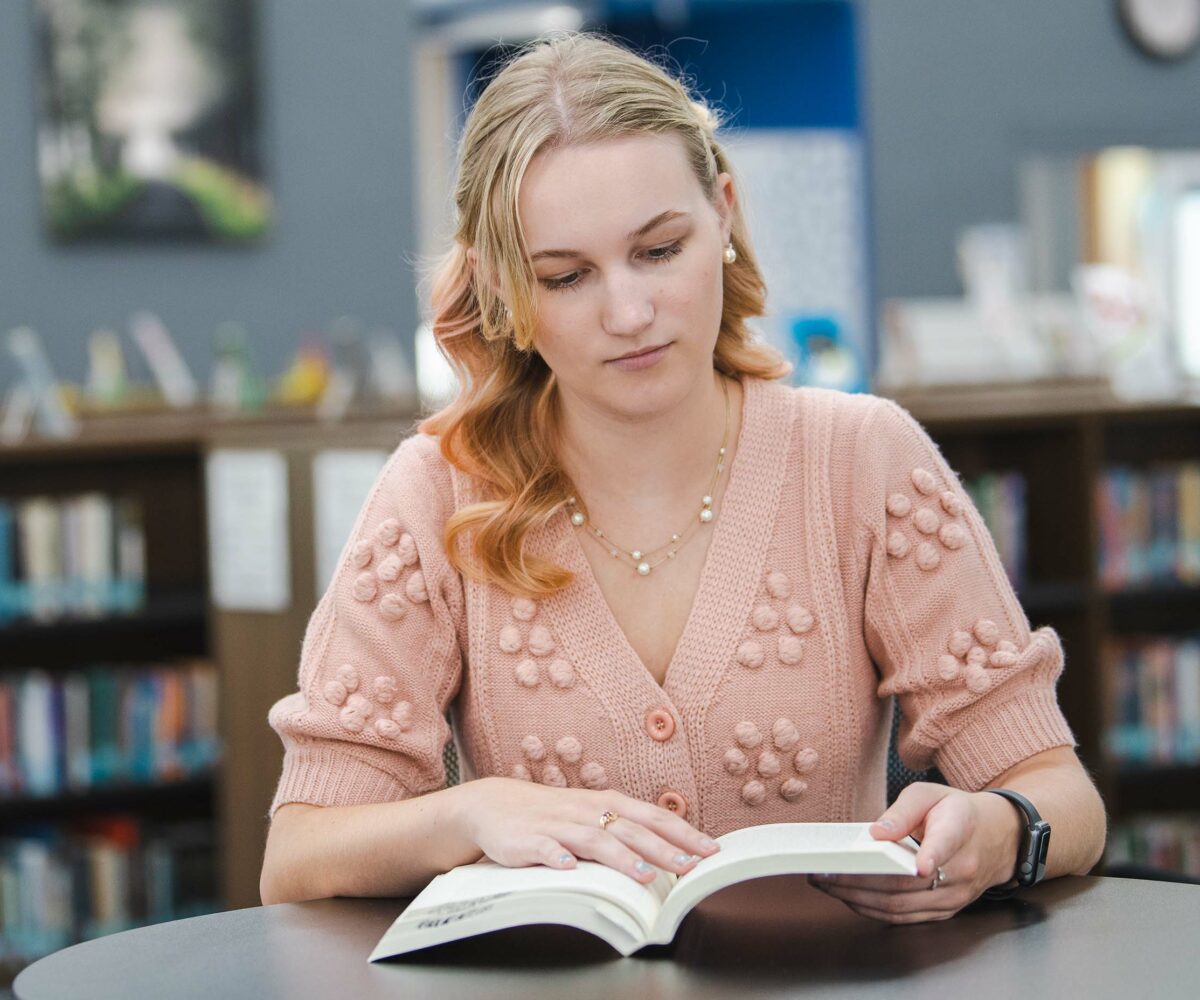 Student in pink sweater reading book in Cottey College library