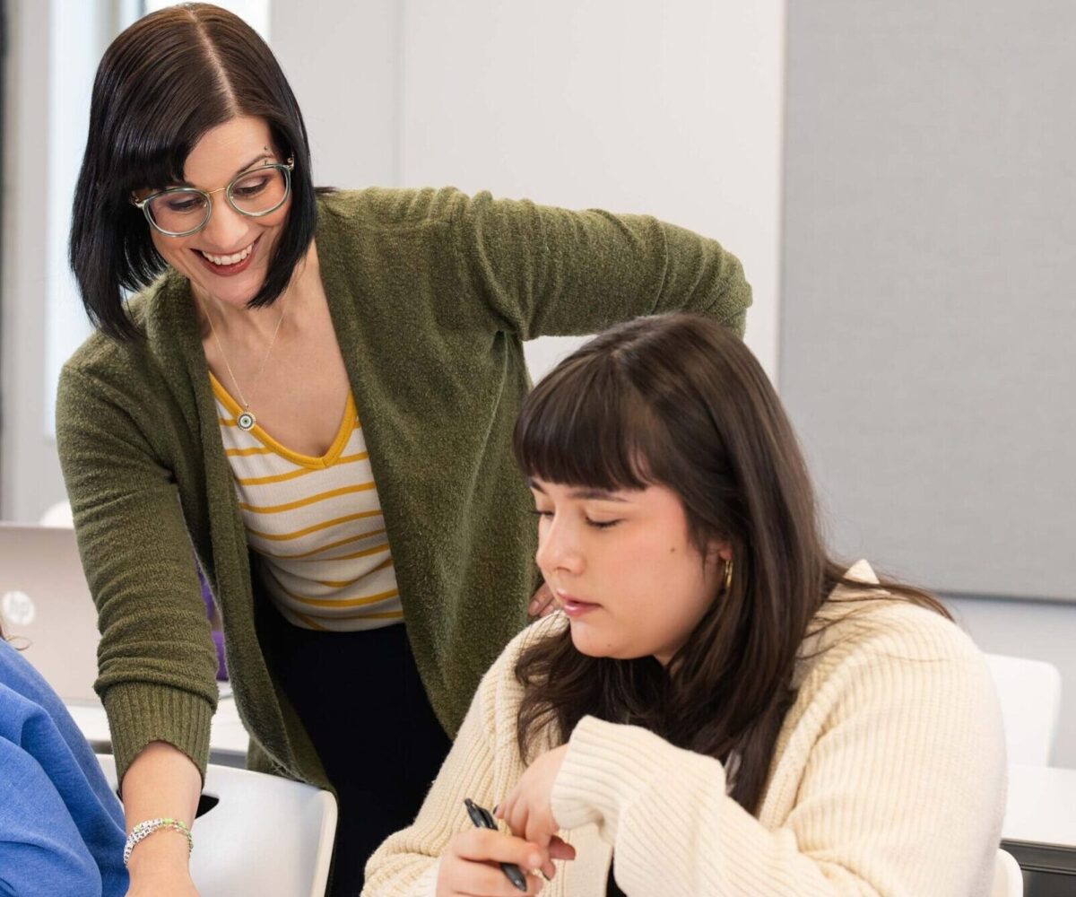 A Cottey professor in a green sweatshirt and glasses helping a student in class.