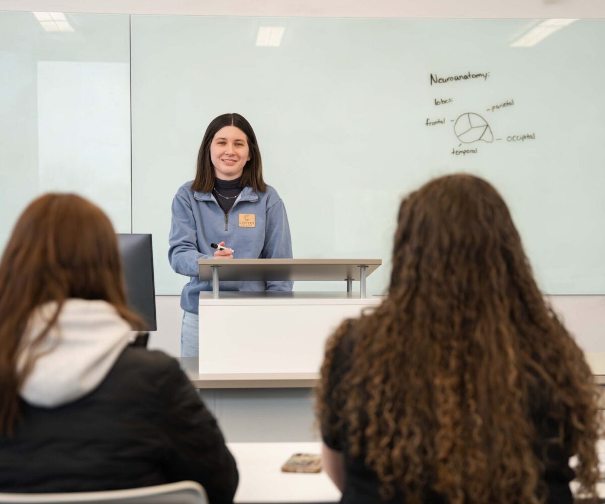 A student giving a presentation in front of a glass whiteboard.