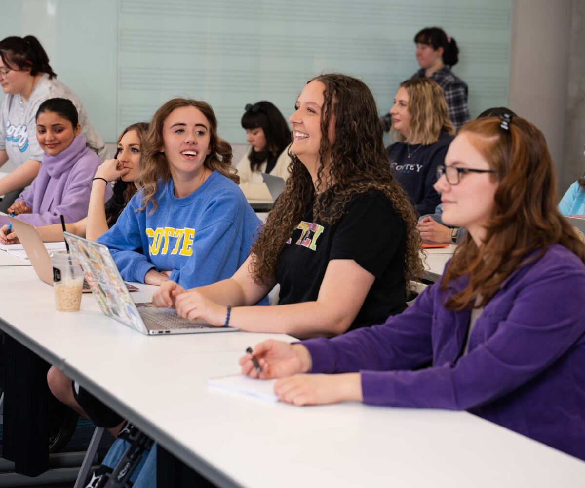A group of college students in class, one is smiling while looking forward.