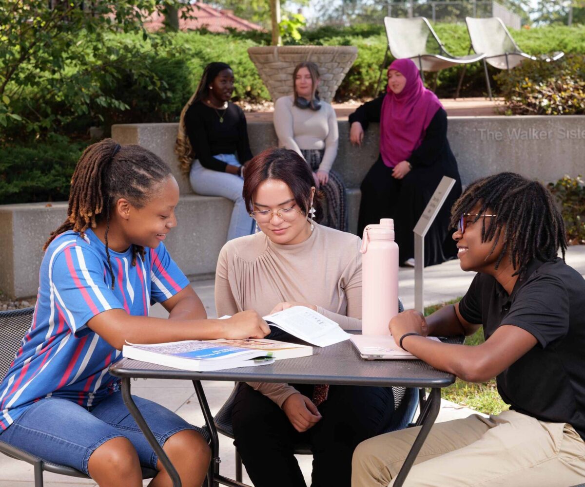 Group of college friends studying around a table in a courtyard.