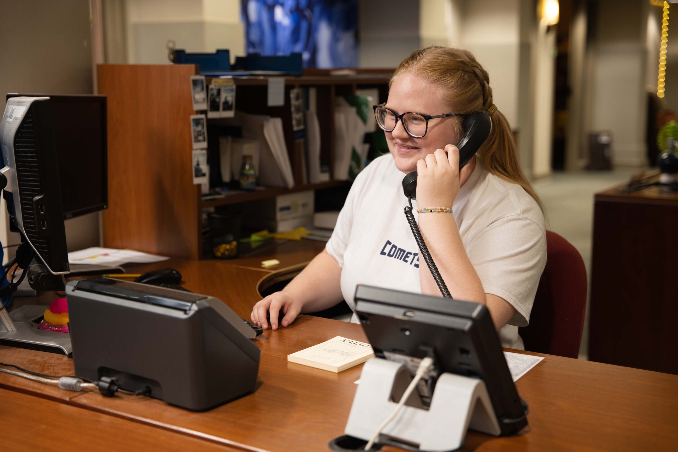 Student answering phones, working an internship in an office surrounded by wooden desks