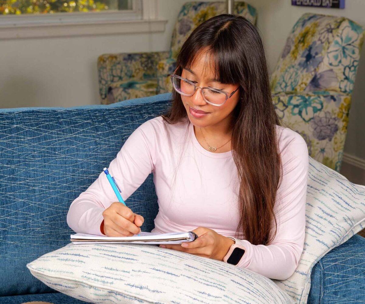 Cottey College student with long hair and glasses studying on the couch in a pink, long-sleeve shirt.