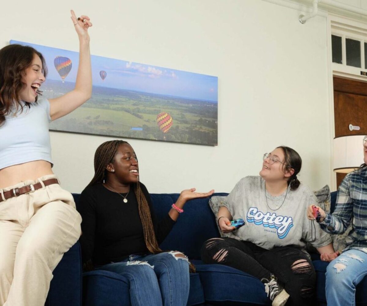 Three Cottey students having fun in their suite living room; one has her hands raised above her head triumphantly.