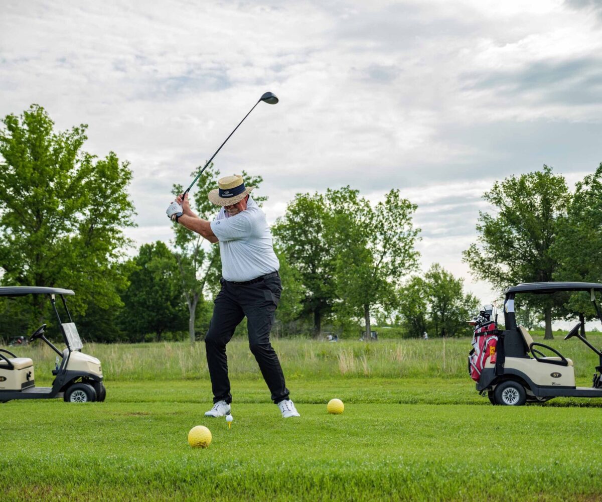Man in white shirt and wide hat swinging a golf club.