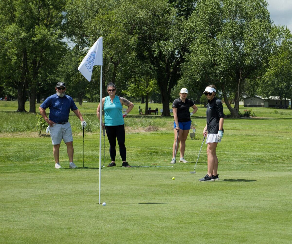 Group of male and female golfers standing around a flag.