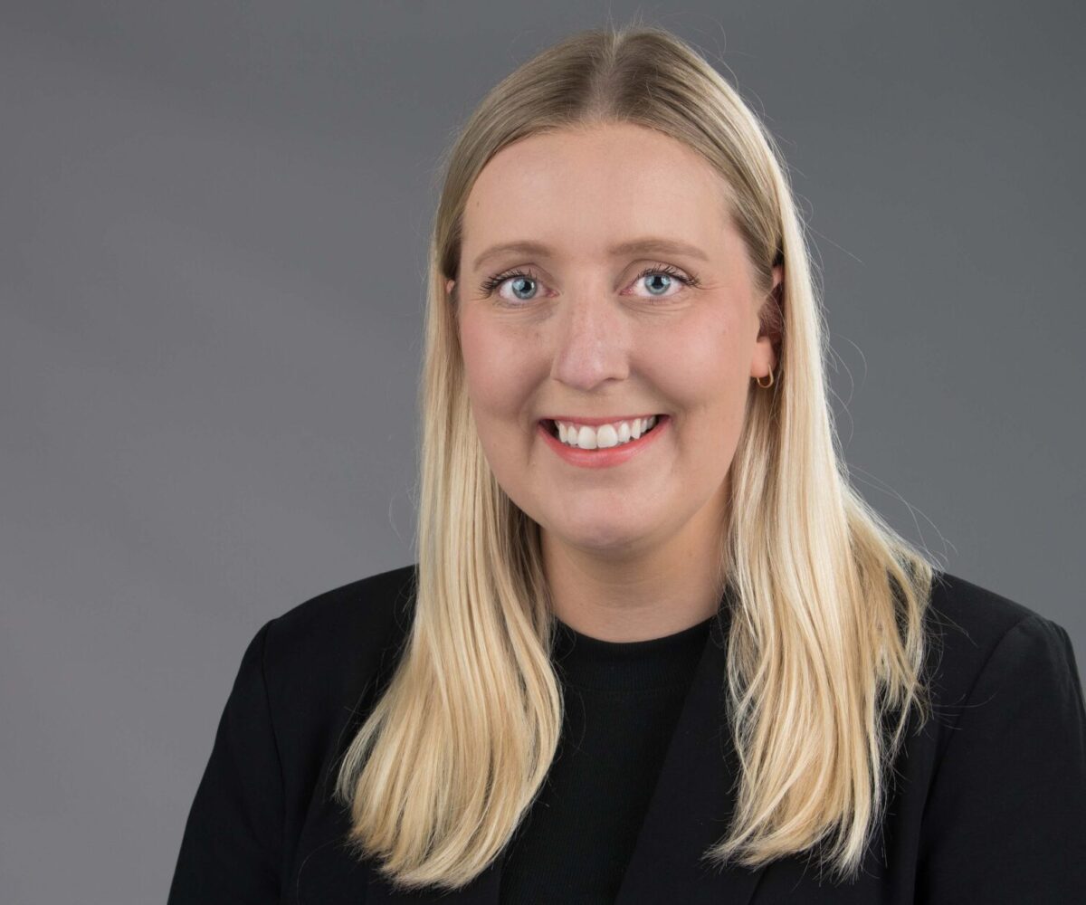 A woman with long, blond hair, a black blouse, and red lipstick smiling.