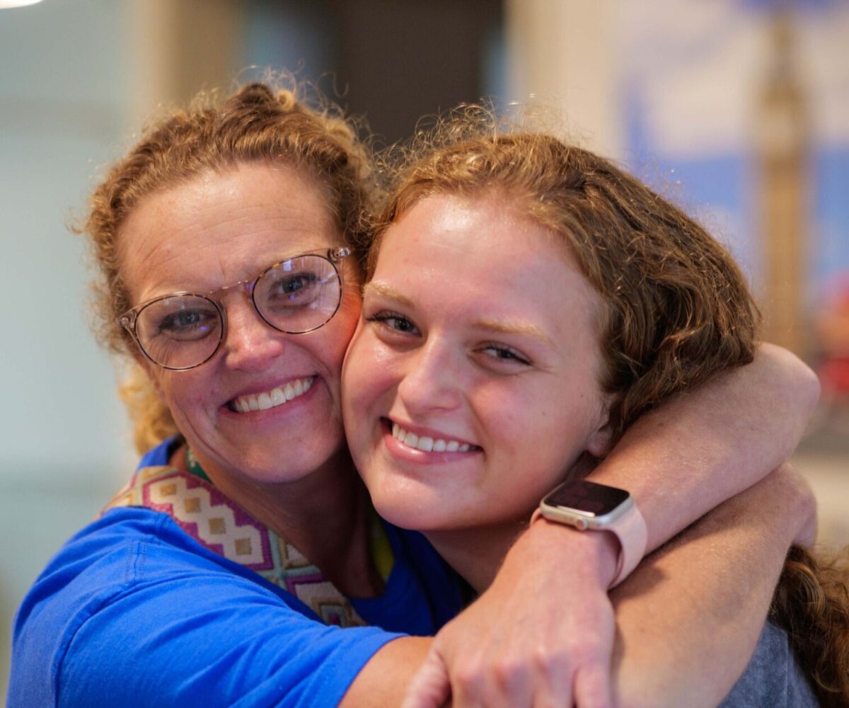 Mother hugging her daughter around the neck.