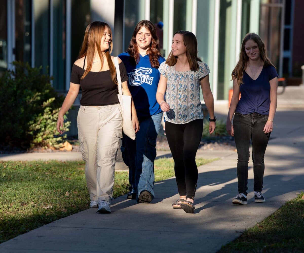 Four Cottey students walking through campus on a path that is covered in patches of shadow and sunlight.