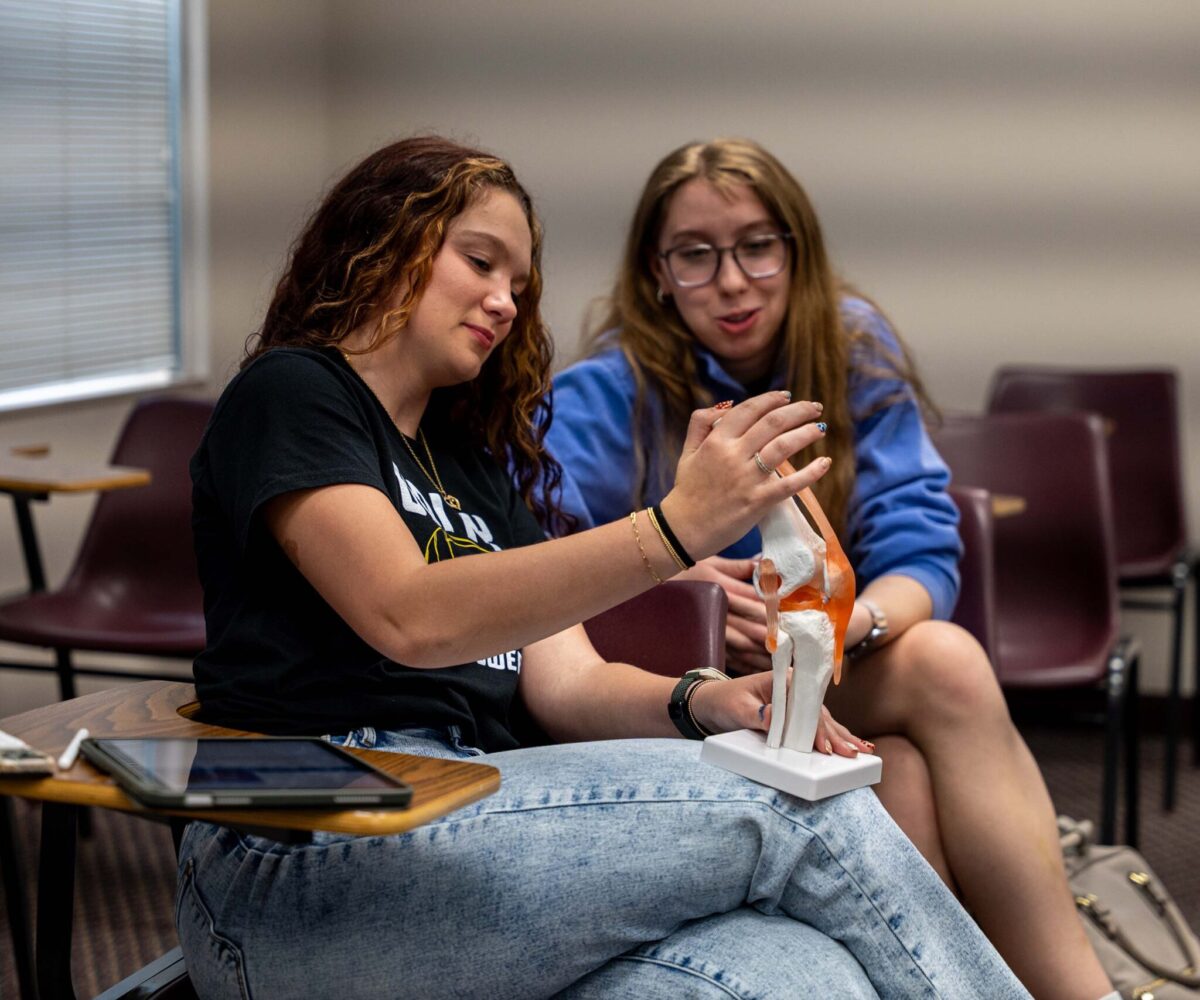 Two students examine a medical model of a knee with great interest.